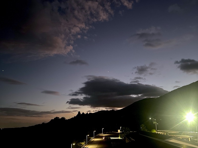 日が落ちたあとの空。雲と山のシルエット、街灯のあかりが見える写真