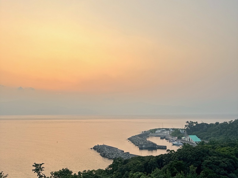 夕方の海と岬。空と海がうすいピンクに染まっている写真