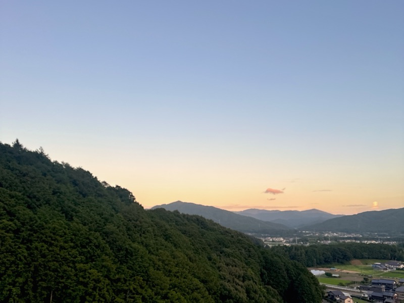 夕暮れの山あいの町を見下ろした写真。空が青からオレンジへ変わっている